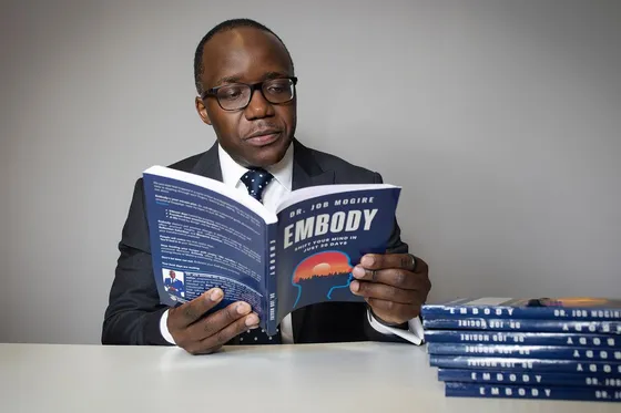 Dr. Job Mogire reading EMBODY beside a stack of copies
