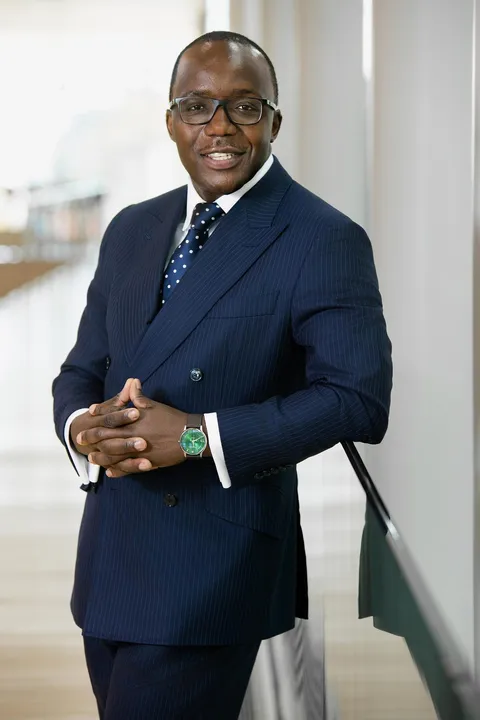 Dr. Job Mogire standing at a stair rail, fingers interlaced, smiling